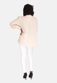 Blusa de color rosa claro, texturizada, con mangas anchas y un pliegue en la espalda, combinada con unos jeans ajustados blancos y tacones negros.