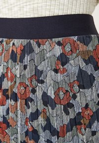 Jupe à motif floral avec une taille en bleu marine. Le design présente des motifs floraux rouges, verts et bleus sur un fond texturé.