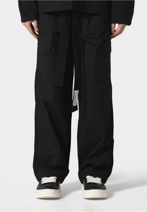 Black cargo pants made from cotton, featuring a loose fit, multiple pockets, a tied waistband, and plain texture, paired with black sneakers.