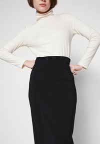 Juoda pieštuko sijonas su prigludusia siluetu, derinamas su smėlio spalvos ilgomis rankovėmis turtleneck'o marškiniais, pagamintais iš minkštos, elastingos medžiagos.