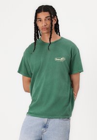 Groene katoenen T-shirt met een ronde 'Denver'-logo op de linkerborst, korte mouwen, relaxed fit en licht verweerde randen.