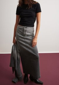 Falda larga de mezclilla gris con cintura alta y cierre frontal de botones, combinada con una camiseta ajustada negra y botines negros.