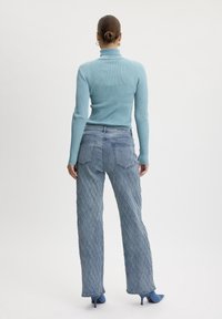 Jasnoniebieski sweter typu turtleneck z prążkowanym wykończeniem, zestawiony z teksturowanymi dżinsami w niebieską, diamentową kratkę oraz niebieskimi czółenkami na szpilce, widok z tyłu.