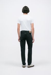 Sorte denimjeans med lige pasform, fem lommer og et lædermærke på bagsiden af taljen, parret med en hvid t-shirt og lyse sko.