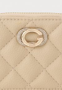 Μπεζ πορτοφόλι από καπιτονέ δέρμα με χρυσό κυκλικό λογότυπο και συνοδευτικά ρινοστάτες. Κλείσιμο με φερμουάρ με ορατές ραφές.