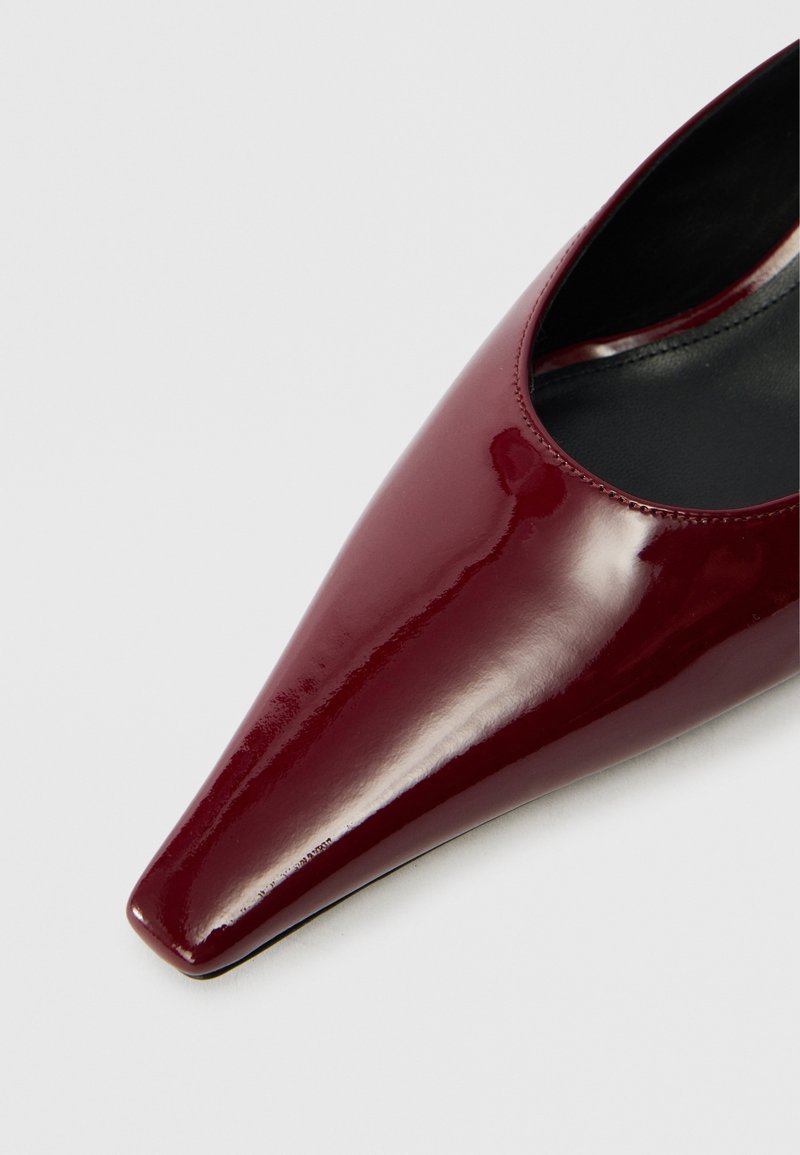 Bordeaux patentlæder pumpe med spids tå og subtile indvendige stikninger. Glat tekstur og minimal design.