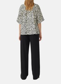 Locker sitzende, kurzärmelige Bluse in Creme mit schwarzen Leopardenflecken, kombiniert mit hoch taillierten schwarzen Hosen mit weitem Bein.
