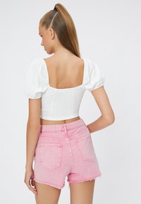 Top corto blanco con fruncido y mangas abullonadas, complementado con unos shorts de mezclilla rosa claro con dobladillos deshilachados y bolsillos traseros.