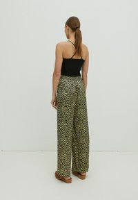 Schwarzes, geripptes Tanktop kombiniert mit weit geschnittenen Hosen im tanfarbenen Leopardenmuster. Die Hose hat einen elastischen Bund und eine glatte Textur.