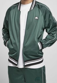 Grüne Satin-Bomberjacke mit weißem Besatz, mit einem Reißverschluss, gerippten Bündchen und Saum sowie einem Logo-Patch auf der Brust.