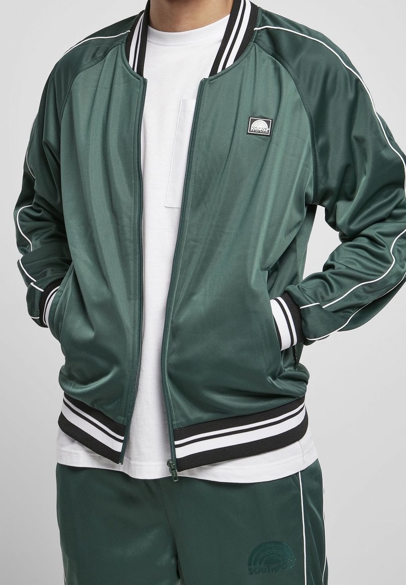 Grüne Satin-Bomberjacke mit weißem Besatz, mit einem Reißverschluss, gerippten Bündchen und Saum sowie einem Logo-Patch auf der Brust.