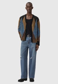 Ζακέτα από μάλλινο μείγμα σε καφέ, μπλε και μαύρα διαμαντένια σχέδια, συνδυασμένη με σκισμένα ανοιχτό μπλε τζιν και μαύρα παπούτσια. Σχεδιασμός με κουμπιά μπρ οστά.