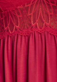 Abito rosso caratterizzato da un corpino in pizzo texturizzato con motivi floreali e una gonna in tessuto liscio e arricciato. In generale, una tonalità vivace e uniforme.