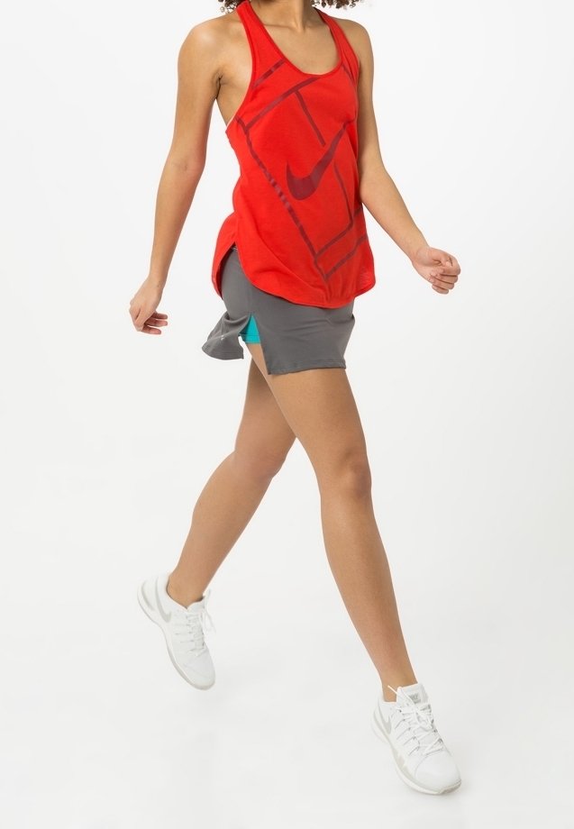 Tirantes rojos de Nike con un patrón geométrico, combinados con pantalones cortos grises con acentos en azul claro. Zapatillas deportivas blancas completan el aspecto.