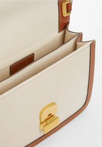 Borsa a tracolla in tela beige con rifiniture in pelle marrone. Caratterizzata da una chiusura in oro e tasche interne. Linee pulite e forma strutturata.