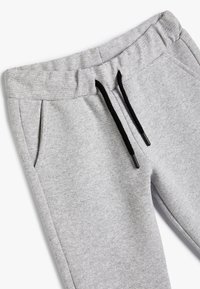 Pantalones de chándal grises hechos de un material suave, con una cinturilla elástica, cordones negros y bolsillos laterales. Textura suave con un diseño minimalista.