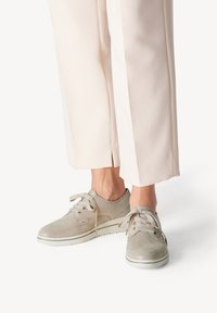 Sneaker in pelle scamosciata grigia con design a stringhe, punta rotonda e suola in gomma chiara, abbinate a pantaloni beige a gamba larga.