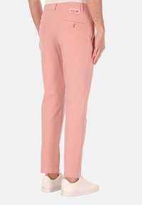 Lichtroze broek met een slim fit, voorzien van een ritszak achterop en een merkband aan de taille. Gestyld met witte sneakers.