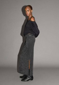 Svart off-shoulder tröja, lång mörkgrå kjol med sidosprund, textil med struktur, kombinerad med svarta ankelstövlar. Enkel, modern design.