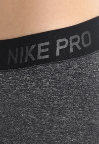 L'elastico in vita nero di Nike Pro presenta lettere riflettenti. Il tessuto è una miscela grigia testurizzata con un motivo mélange.