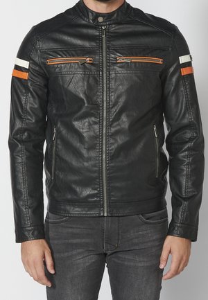 Schwarze Lederjacke mit Frontreißverschluss, orange-weißen Streifen an den Ärmeln, orangefarbenen Reißverschlussdetails auf der Brust, getragen zu dunklen Jeans.