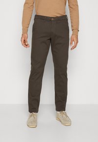 Brown pants made of cotton, slim fit design with a button closure, side pockets, and a smooth texture. Paired with beige suede shoes.