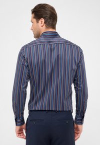 Camicia a righe con strisce verticali in navy, rosso e blu; maniche lunghe; e colletto classico. Vestibilità slim, dettaglio con bottoni ai polsini.