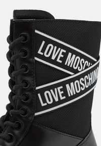 Mustad musteel lakkimisega saapad, millel on matt nahk, võrgusilma ülemine osa ja kontrastsed valged "LOVE MOSCHINO" ribaad varre ümber, et lisada detaili.