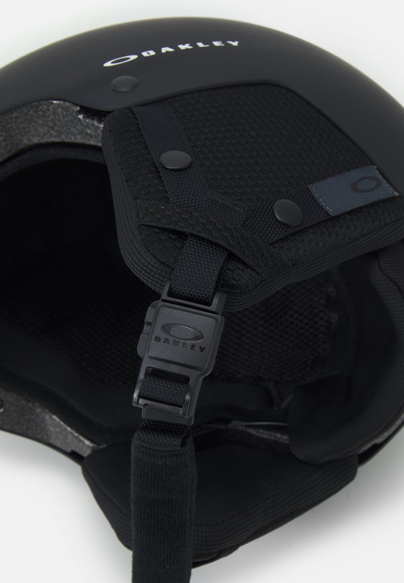 Svart hjälm med matt finish, tygfoder, justerbart hakband och framträdande Oakley-logotyp på toppen.