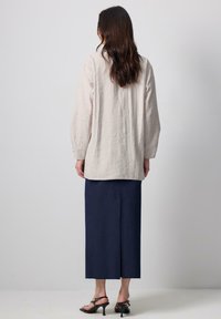 Light beige linen top with long sleeves, paired with a navy blue knee-length skirt featuring a back slit. Black heeled sandals complete the look.