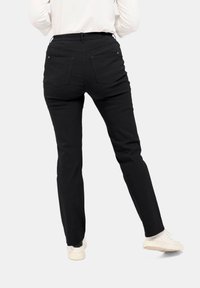 Zwarte tapered broek met een gladde textuur, twee achterzakken en een elastische tailleband, gecombineerd met witte sneakers.