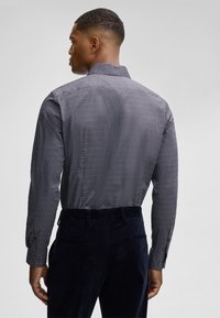 Camicia a maniche lunghe di colore blu navy con un motivo geometrico bianco. Presenta un colletto con bottoni e un tessuto testurizzato, abbinata a pantaloni in velluto a coste scuri.