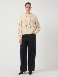 Cremefarbener, gestrickter Pullover mit Lochmuster und mehrfarbigen Akzenten; kombiniert mit hoch taillierten schwarzen, weiten Jeans und spitzen schwarzen Schuhen.