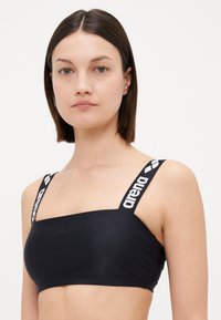Black swim crop top with wide straps featuring "arena" branding. Smooth texture, cropped design, and square neckline.
