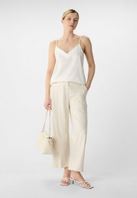 White satin camisole with adjustable straps, paired with cream wide-leg trousers, white strappy heels, and a small cream handbag.
