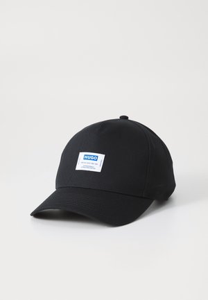 Casquette de baseball noire à visière courbée avec une étiquette rectangulaire blanche portant le texte "HUGO" en bleu au centre avant.