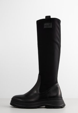 Knee-high black boots with a textured leather base and smooth fabric shaft. Features a thick rubber sole and a pull tab at the rear.
