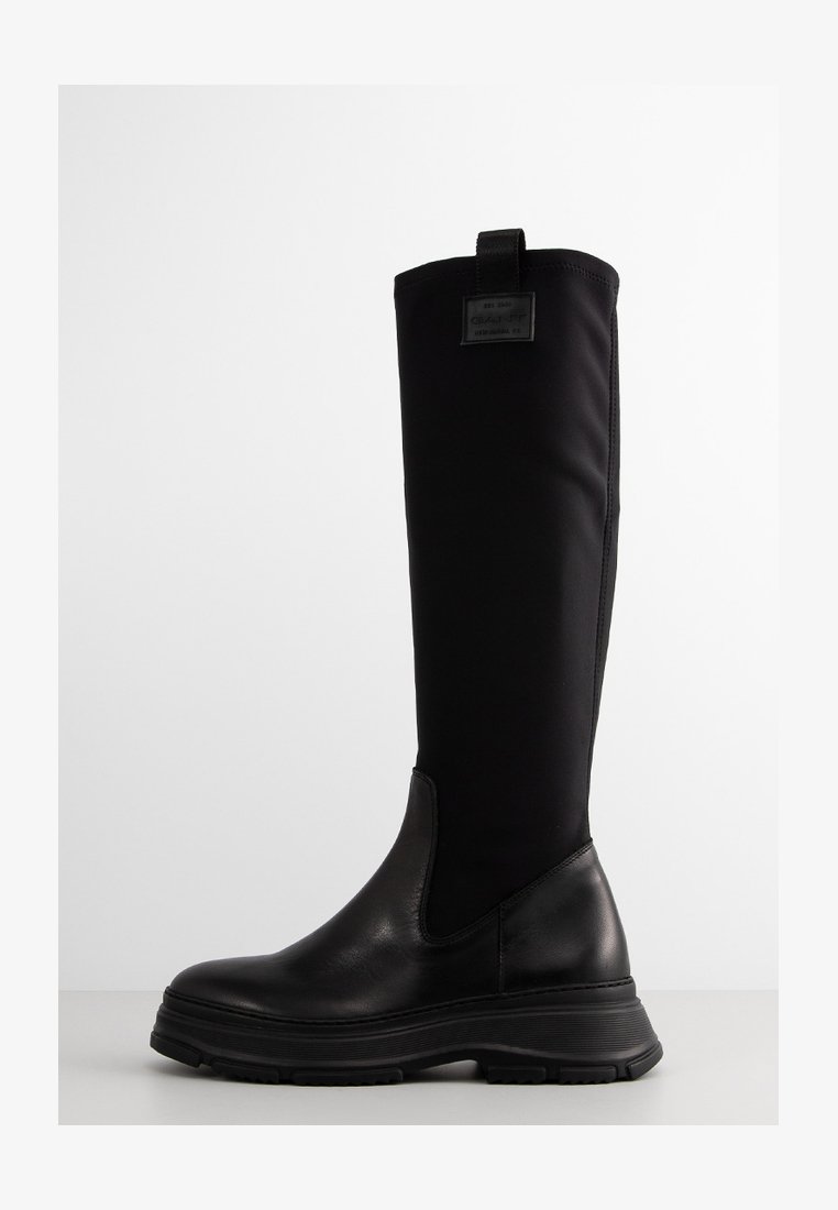 Knee-high black boots with a textured leather base and smooth fabric shaft. Features a thick rubber sole and a pull tab at the rear.