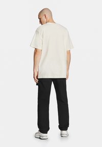 Jasnobeżowa bawełniana koszulka o luźnym kroju, z krótkimi rękawami i okrągłym dekoltem, w połączeniu z czarnymi spodniami o luźnym kroju i białymi sneakersami.