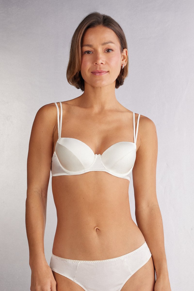 Vit, slät tyg-bh med tunna justerbara band och rundad koppdesign. Mjuk textur med en central rosettdetalj. Matchande vita trosor.
