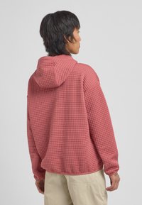 Rózsaszín, oversized kapucnis pulóver, texturált anyagból készült, steppelt mintával; húzózsinórral ellátott kapucnival és laza fazonnal rendelkezik.