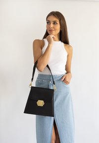 Borsa a tracolla in pelle nera con una chiusura esagonale dorata, design strutturato e una singola tracolla. Presenta una texture liscia e uno stile minimalista.
