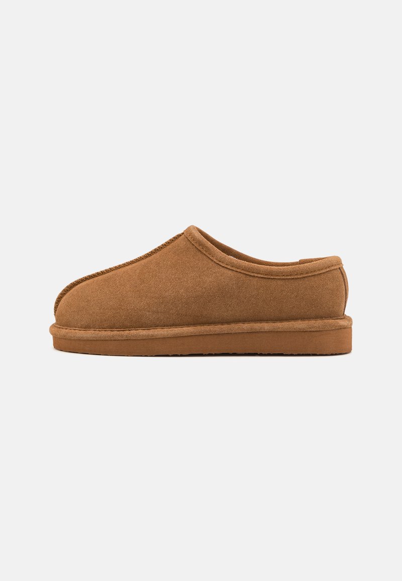 Chausson en suede marron avec un bout arrondi, un dos bas et une tige texturée. Il présente une couture et une semelle en caoutchouc plate pour un usage intérieur.