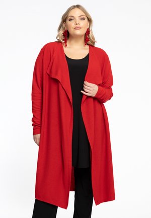 Langer, offener Cardigan in lebhaftem Rot, aus weichem Stoff mit langen Ärmeln und fließender Silhouette. Kombiniert mit einem schwarzen Oberteil.