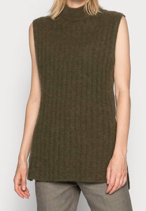 Pull sans manches côtelé vert olive foncé avec un col montant porté avec un pantalon gris, montrant le haut du corps et les bras.
