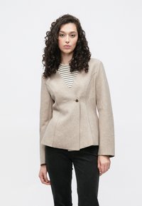 Lichtbeige jas van een wolmengsel met een V-hals, één knoopsluiting en een peplum taille. Gestreept shirt eronder, gedragen met donkere broek.