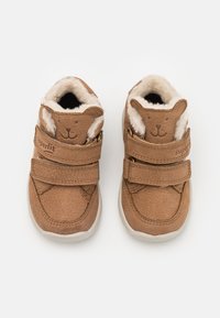 Chaussures en cuir marron pour tout-petits avec un doux revêtement beige, présentant un design de visage d'ours sur la languette et deux bandes Velcro ajustables.