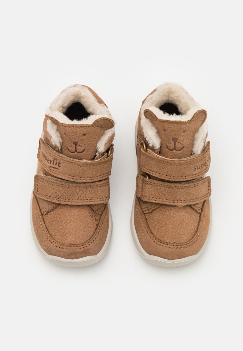 Chaussures en cuir marron pour tout-petits avec un doux revêtement beige, présentant un design de visage d'ours sur la languette et deux bandes Velcro ajustables.