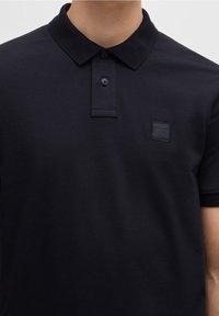 Polo bleu marine en coton, doté d'un col plié, d'une patte à deux boutons et d'un écusson carré avec logo sur la poitrine gauche.