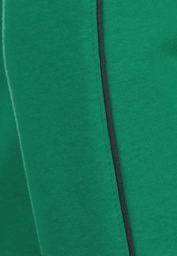 Zelená sportovní tkanina s texturovaným povrchem, se černým lemem podél švu pro kontrast.